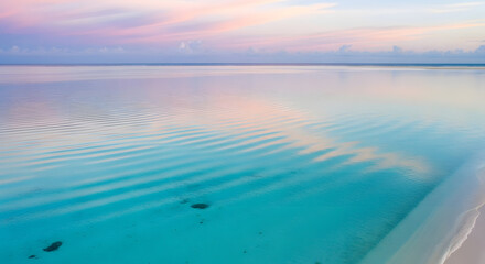 Fototapeta premium Vibrant pastel sky reflected on the serene turquoise tropical ocean, with gentle ripples on the calm water at sunrise or sunset, creating a peaceful paradise scene