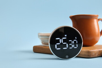 Modern kitchen timer, wooden cutting board and dishware on blue background