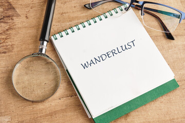 A well-used wooden table holds a notepad titled Wanderlust, accompanied by a magnifying glass and glasses, inviting exploration and adventure in travel writing