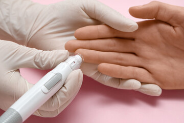Doctor with young diabetic woman using lancet pen on pink background, closeup