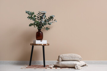 Box and vase with eucalyptus twigs on table near beige wall in room