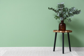 Vase with eucalyptus twigs on stool near green wall in room