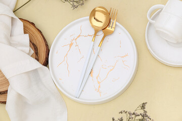 Golden fork with spoon, plate and napkin on beige background