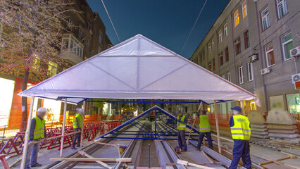 Builders making tent cover over tram rails at the stage of their installation on the road timelapse.
