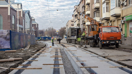 Tram rails at the stage of their unloading from truck by crane on concrete plates on the road...