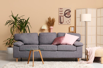 Grey sofa with coral cushions near beige wall in interior of living room