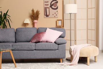 Grey sofa with coral cushions near beige wall in interior of living room