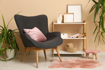 Armchair with coral cushion near beige wall in interior of living room