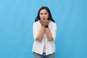 A beaming young Asian woman opens her arms forward, blowing and sending kisses into the air,...