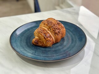 Freshly baked croissant served on blue porcelain plate, breakfast concept. BSD, Indonesia - October, 19 2025