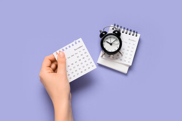 Female hand with calendar and alarm clock on purple background
