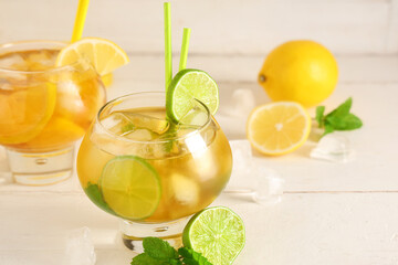 Glasses of cold tea with citrus fruit slices and mint leaves on light wooden background