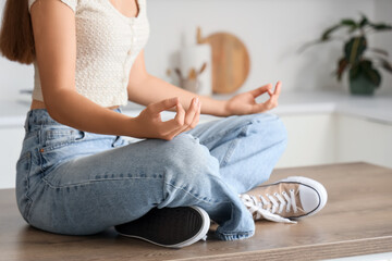 Young woman meditating on table in kitchen, closeup. Zen concept