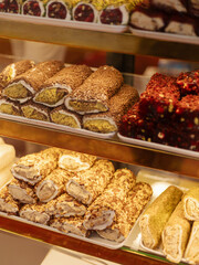 A tempting selection of traditional sweets is arranged in a bakery shop. Various rolled desserts are topped with nuts, showcasing rich colors and textures that invite customers to indulge