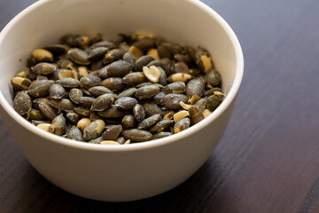 baked pumpkin seeds in small white bowl close up