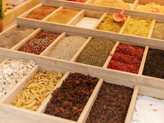 A vibrant selection of spices is arranged in wooden trays at a market. Each tray holds different seasonings, showcasing various colors and textures that attract shoppers