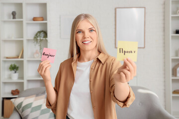 Smiling young woman holding sticky notes with "bonjour" and "привет" for language learning and communication © Pixel-Shot