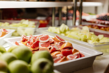 A colorful assortment of sliced and whole fruits is arranged neatly in a buffet setting. This vibrant spread includes melons, apples, and citrus. Perfect for an evening gathering or party