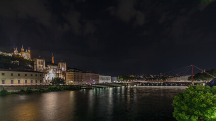 Panorama showing night timelapse of Lyon's cityscape with the red suspension footbridge over the...