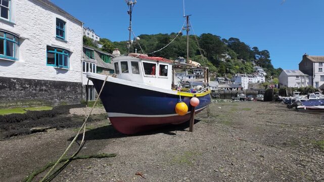 Polperro harbour at low tide. Camera tracks / dollies torwards a fishing boat. It has buoys on. It is summer and sunny. 