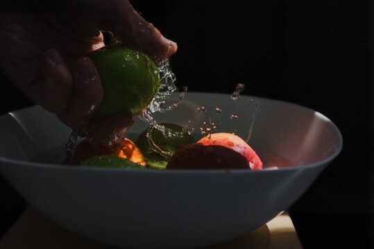 Male hands cleaning apples with a lot of water on black background, closeup photo. Splashing water around apple in hand, healthy food preparation at home