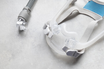 A full face CPAP mask with its headgear straps shot over a grey textured background. The mask is used to give therapy to patiences who have been diagnosed with sleep apnea.