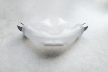 Nasal pillow CPAP masks attachment shot over a grey textured background. The mask is used to give therapy to patiences who have been diagnosed with sleep apnea.