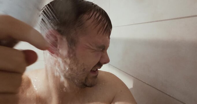 A man stands in the shower rinsing his ears with running water, wincing slightly as the water pressure hits. The clip shows a realistic and relatable hygiene moment during daily shower routine.