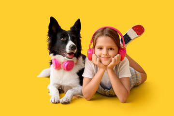 Cute little girl and Border Collie dog with headphones lying on yellow background