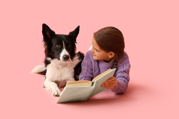 Cute little girl with Border Collie dog reading book on pink background