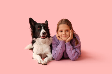 Cute little girl with Border Collie dog lying on pink background