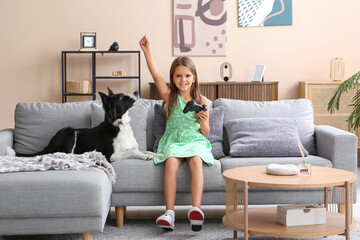 Happy little girl with Border Collie dog playing video game on sofa at home