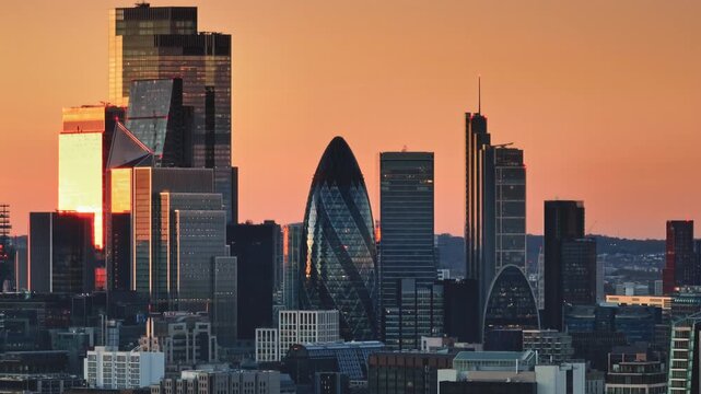 United Kingdom, London: Illuminating warm sunset colors over London's modern cityscape, highlighting iconic skyscrapers like the Gherkin in a stunning panorama. Drone flight footage