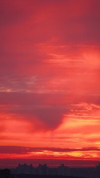 Vertical video of bright red sunrise over city on cloudy day. Temperature inversion and Rayleigh scattering phenomena.