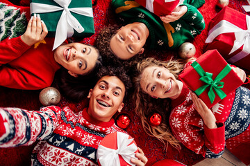 Group of friends celebrating Christmas together with presents and festive sweaters on a joyful and merry winter evening