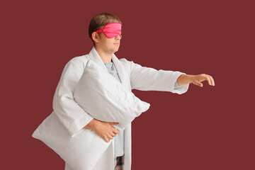 Male sleepwalker in pajamas with pillow on burgundy background