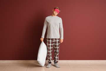 Male sleepwalker in pajamas with pillow near burgundy wall