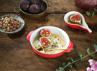 A close-up of figs, cut in half and sprinkled with pistachios, sitting in a bowl of cream sauce with a golden spoon