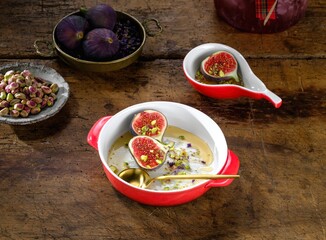 Close-up showcases bowls and dishes filled with halved figs. They are garnished with pistachios, drizzled with honey, and sprinkled with dried lavender on a dark wooden table