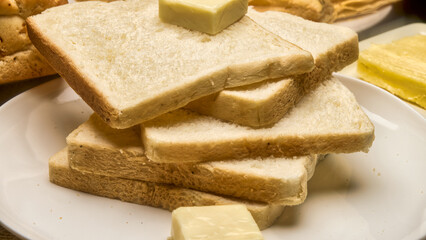 A detailed close-up image of soft, freshly baked white bread slices stacked neatly on a plate with a cube of butter on top. The warm tones and texture highlight freshness and comfort, ideal for bakery