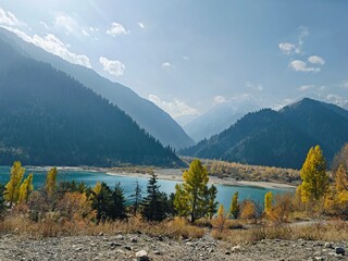 Issyk Lake in Kazakhstan during autumn. The turquoise mountain lake surrounded by colorful autumn forest and majestic peaks © SV