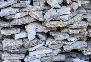 A detailed full-frame shot of a wall or pile constructed from flat, rough-cut gray and yellowish limestone rocks stacked haphazardly on top of each other, forming a rustic texture.