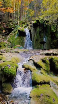 Small mountain waterfall surrounded by moss and autumn leaves, captured by a static camera in calm forest atmosphere