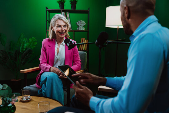 Group of hosts is capturing a live audio broadcast, engaging in a lively, amusing conversation around microphones and a laptop in a professional studio setting