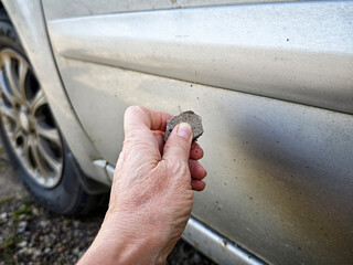 Vandalism act as a teenager scratches a car with a stone in a parking lot