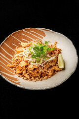 Traditional Pad Thai with chicken, rice noodles, bean sprouts, peanuts, and lime in a ceramic bowl on black background. Authentic Thai cuisine in vibrant, appetizing presentation.