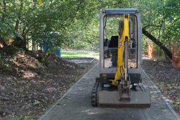 Mini excavator parked on a narrow pathway surrounded by trees, used for small-scale construction work.