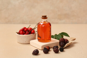 Bottle of cosmetic rose hip oil and bowl with berries on beige background