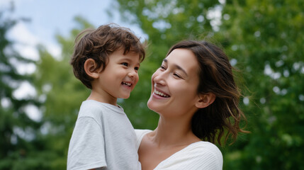 Fototapeta premium Happy mother lifting her son outdoors, both smiling and laughing together, bright natural light, green trees and blue sky in background, joyful family bonding moment, love and conn