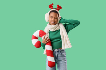 Teenage African-American girl in Christmas reindeer horns with candy cane pillow on green background